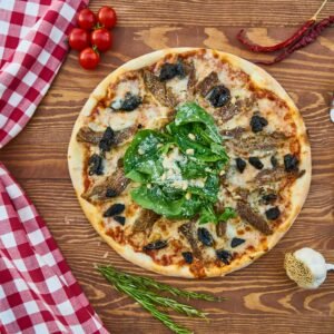 Delicious Italian pizza topped with greens and served on a rustic wooden table with a red checkered napkin.
