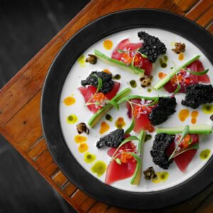 Aerial view of gourmet dish featuring caviar and vibrant garnishes on a wooden table.